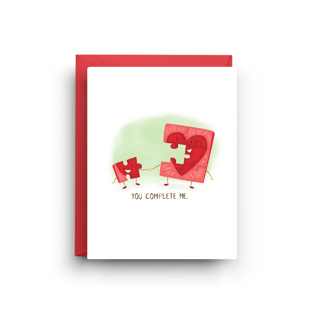 Greeting card with two puzzle pieces holding hands and 'You Complete Me' text on a white background.